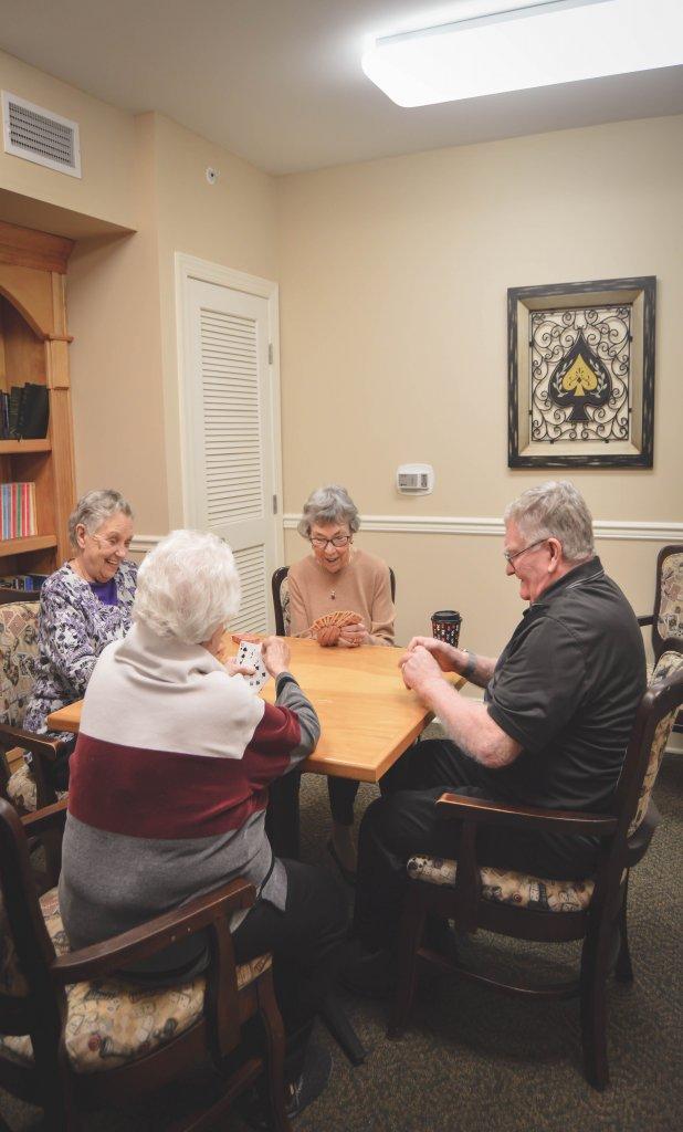4 residents seat and playing card games in entertainment lounge