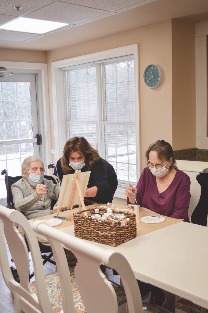 caregiver helping 2 woman residents with their paintings