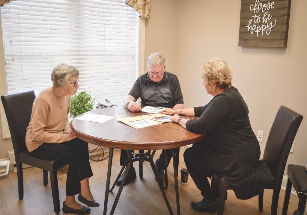 elderly couple meeting with coordinator at round table reviewing documents