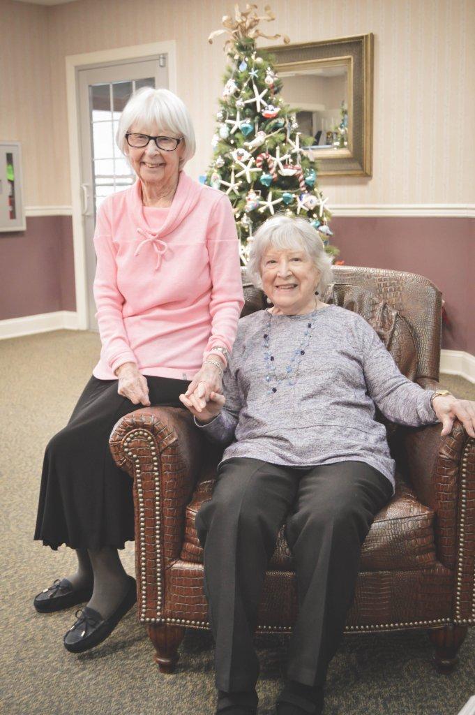 2 smiling independent living residents pose in chair in front of christmas tree