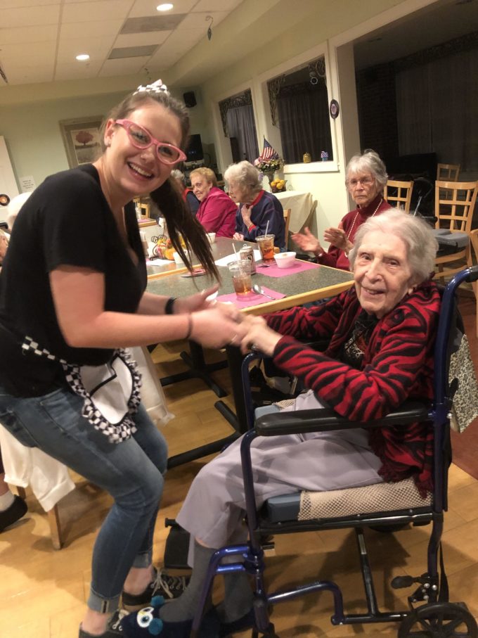 smiling standing woman caregiver holding the hands of a woman resident in wheelchair